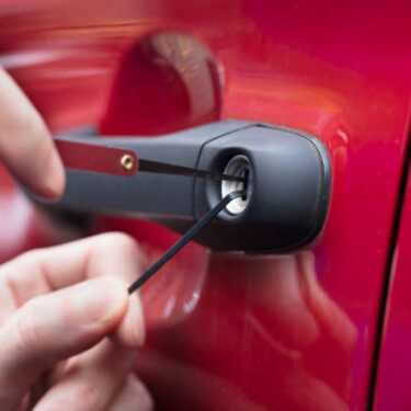 Close-up Of A Human Hand Opening Red Car's Door With Lockpicker